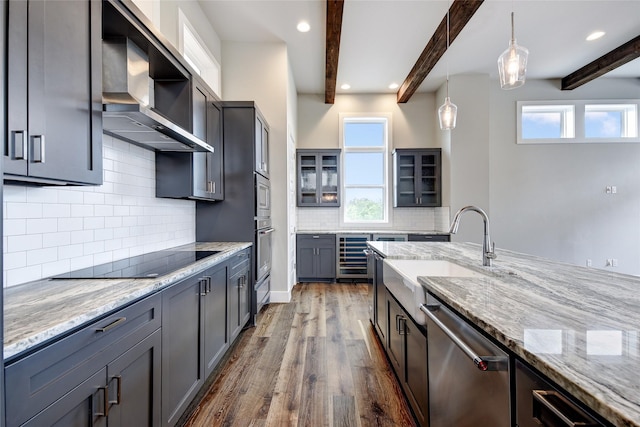 kitchen with sink, decorative light fixtures, appliances with stainless steel finishes, beam ceiling, and wall chimney range hood