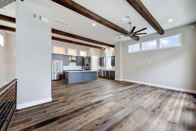 unfurnished living room featuring beamed ceiling, plenty of natural light, dark hardwood / wood-style floors, and ceiling fan