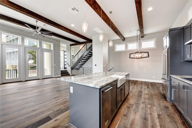 kitchen with high end refrigerator, beam ceiling, a kitchen island with sink, and hanging light fixtures