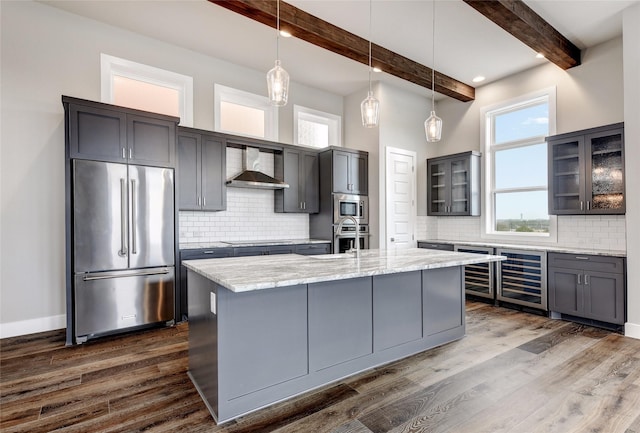 kitchen with beamed ceiling, wine cooler, hanging light fixtures, stainless steel appliances, and wall chimney exhaust hood