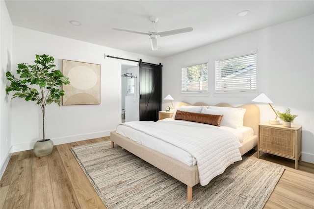 bedroom featuring hardwood / wood-style flooring, a barn door, and ceiling fan