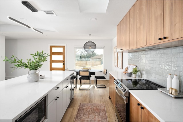 kitchen featuring wine cooler, white cabinets, stainless steel electric range oven, decorative light fixtures, and light wood-type flooring