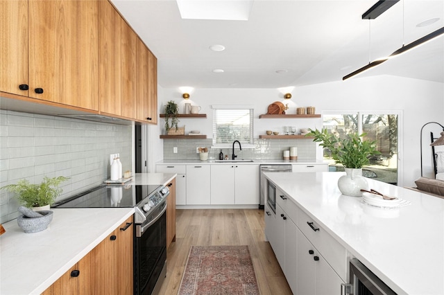 kitchen with stainless steel electric range oven, a skylight, sink, dishwashing machine, and white cabinets