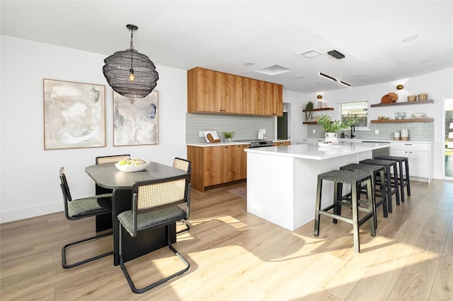 kitchen featuring sink, light wood-type flooring, a kitchen island, pendant lighting, and backsplash