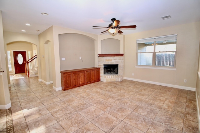 unfurnished living room featuring ceiling fan and a stone fireplace