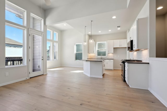 kitchen with stainless steel range with gas cooktop, pendant lighting, white cabinets, decorative backsplash, and a center island