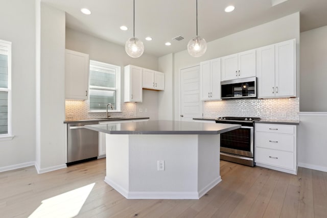 kitchen with a kitchen island, sink, white cabinets, hanging light fixtures, and stainless steel appliances