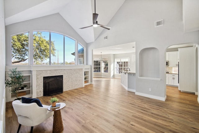 living room with ceiling fan, a tiled fireplace, light hardwood / wood-style floors, and a wealth of natural light