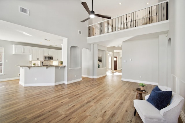 living room with ceiling fan, light hardwood / wood-style flooring, and a high ceiling