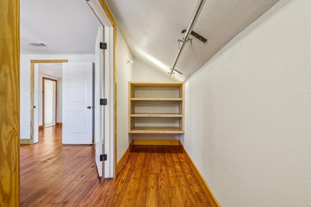 hallway featuring lofted ceiling, wood-type flooring, and a textured ceiling