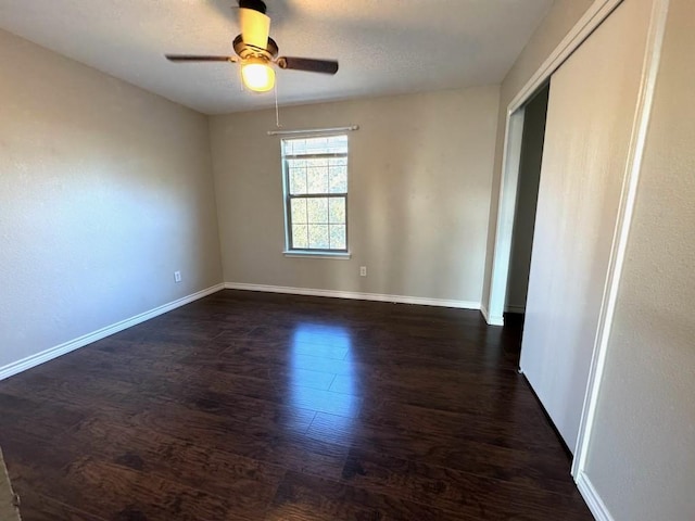 empty room with dark wood-type flooring, baseboards, and ceiling fan