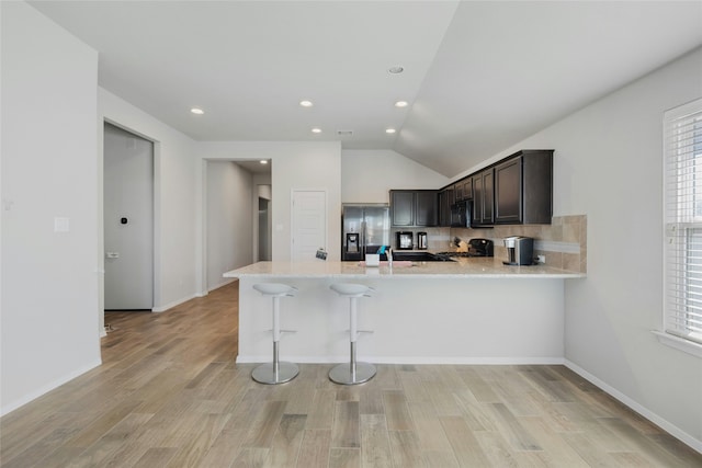 kitchen featuring lofted ceiling, stainless steel fridge with ice dispenser, light hardwood / wood-style flooring, kitchen peninsula, and decorative backsplash