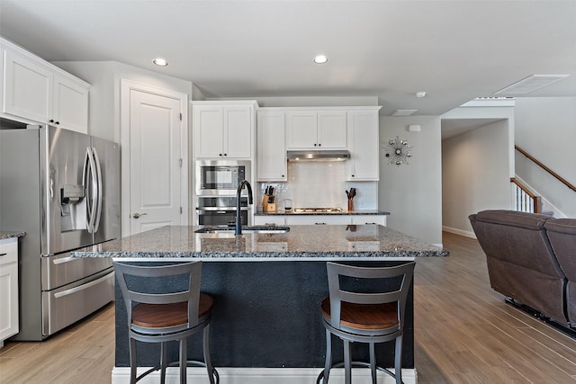 kitchen featuring white cabinets, appliances with stainless steel finishes, a kitchen island with sink, and dark stone counters