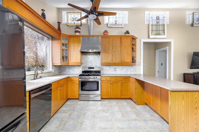 kitchen featuring stainless steel gas stove, sink, black dishwasher, kitchen peninsula, and wall chimney range hood