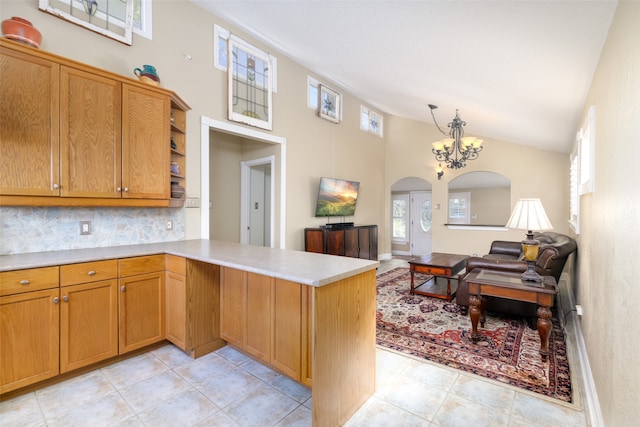 kitchen with high vaulted ceiling, kitchen peninsula, a notable chandelier, pendant lighting, and decorative backsplash