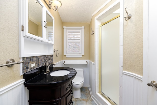 bathroom with vanity, toilet, a shower with shower door, and a textured ceiling