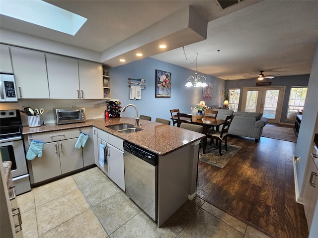 kitchen with sink, kitchen peninsula, stone counters, pendant lighting, and stainless steel appliances