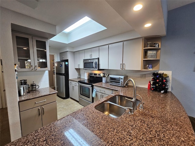 kitchen with appliances with stainless steel finishes, tasteful backsplash, sink, dark stone countertops, and kitchen peninsula