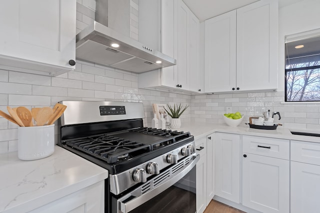 kitchen with stainless steel gas stove, tasteful backsplash, white cabinetry, light stone countertops, and wall chimney exhaust hood