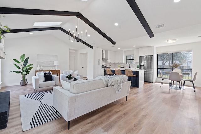 living room with an inviting chandelier, sink, vaulted ceiling with skylight, and light hardwood / wood-style floors