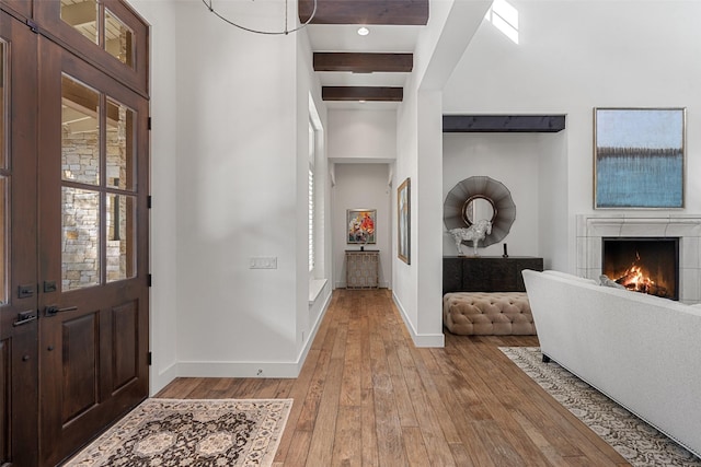 entrance foyer featuring beam ceiling, a tile fireplace, and light hardwood / wood-style floors