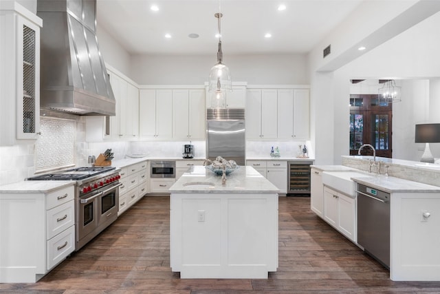 kitchen with high end appliances, white cabinetry, premium range hood, and a center island with sink