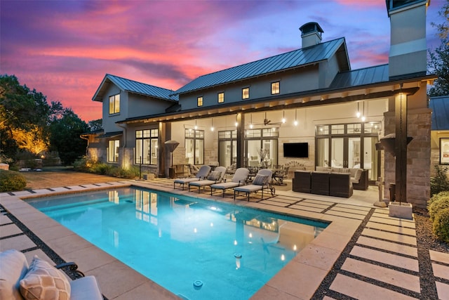 pool at dusk featuring ceiling fan, an outdoor living space, and a patio