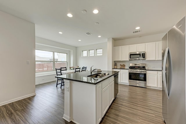 kitchen featuring dark wood-type flooring, stainless steel appliances, an island with sink, and white cabinets