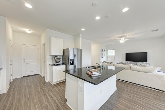 kitchen featuring sink, wood-type flooring, stainless steel fridge with ice dispenser, a center island with sink, and white cabinets