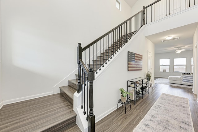 stairway with hardwood / wood-style floors, a towering ceiling, and ceiling fan