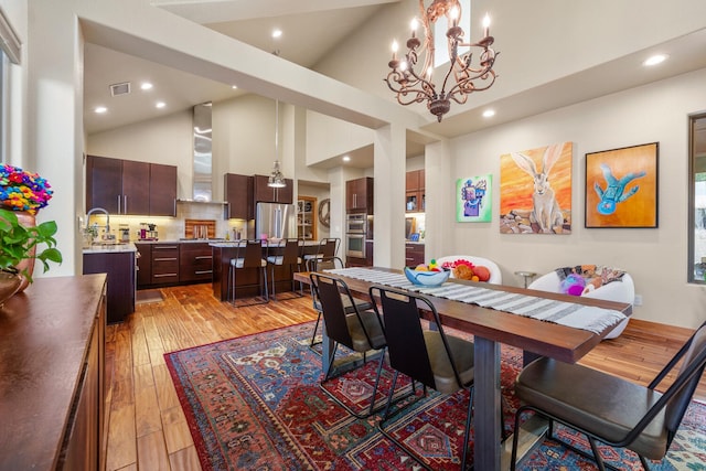 dining area with an inviting chandelier, high vaulted ceiling, and light wood-type flooring