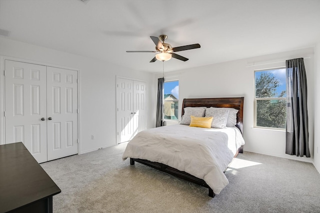 bedroom featuring two closets, light colored carpet, and ceiling fan