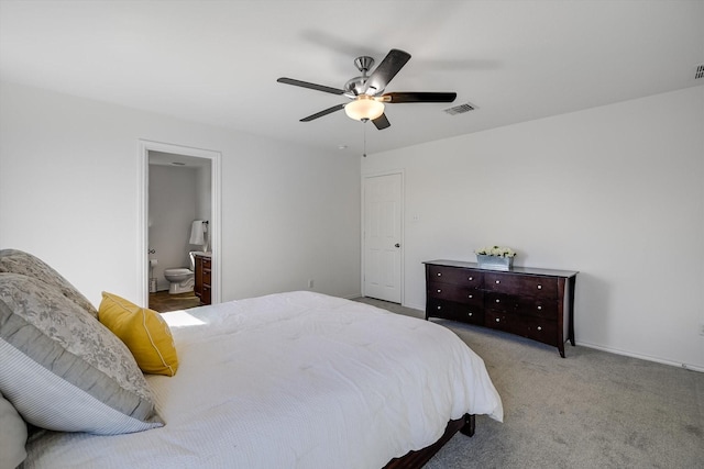 bedroom with ceiling fan, light colored carpet, and ensuite bath