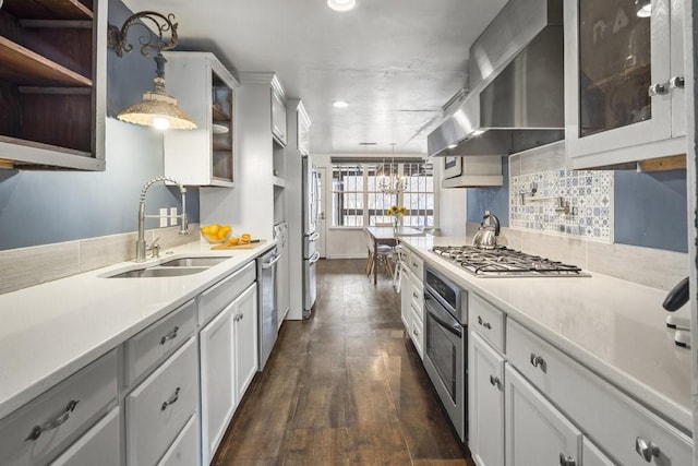 kitchen with sink, appliances with stainless steel finishes, hanging light fixtures, range hood, and white cabinets