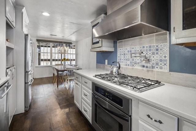 kitchen featuring white cabinetry, decorative light fixtures, appliances with stainless steel finishes, dark hardwood / wood-style flooring, and wall chimney range hood