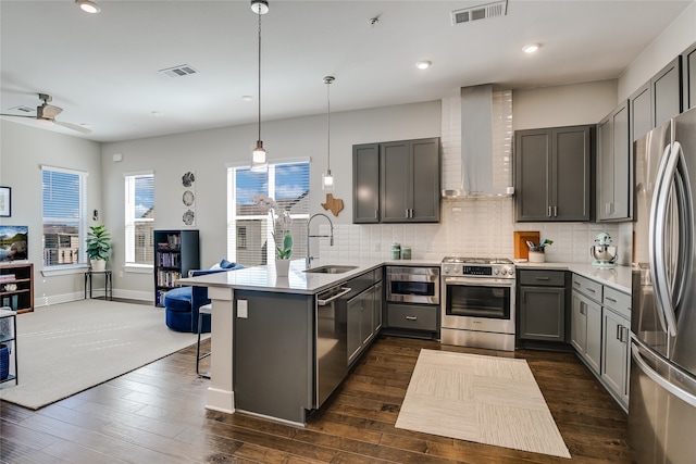 kitchen with appliances with stainless steel finishes, decorative light fixtures, gray cabinetry, kitchen peninsula, and wall chimney exhaust hood