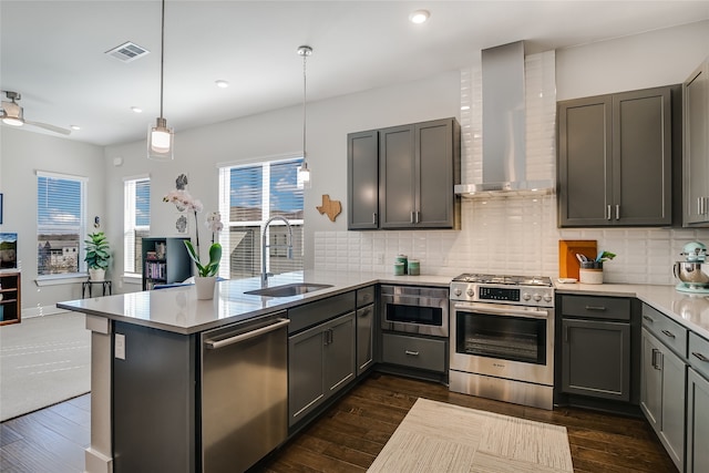 kitchen featuring sink, hanging light fixtures, appliances with stainless steel finishes, decorative backsplash, and wall chimney range hood