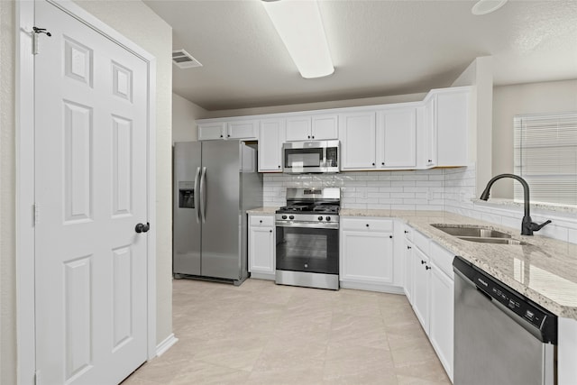 kitchen with sink, white cabinets, stainless steel appliances, light stone countertops, and backsplash