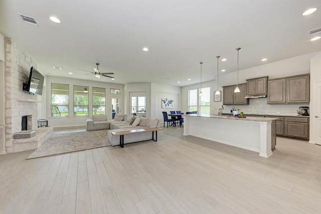 living room featuring sink, a stone fireplace, light hardwood / wood-style floors, and ceiling fan