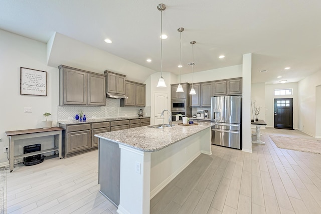 kitchen with sink, light stone counters, an island with sink, pendant lighting, and stainless steel appliances