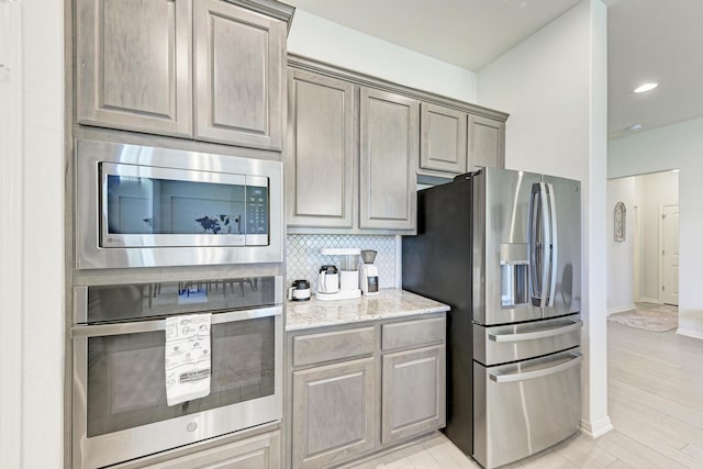 kitchen featuring stainless steel appliances, light stone countertops, and decorative backsplash