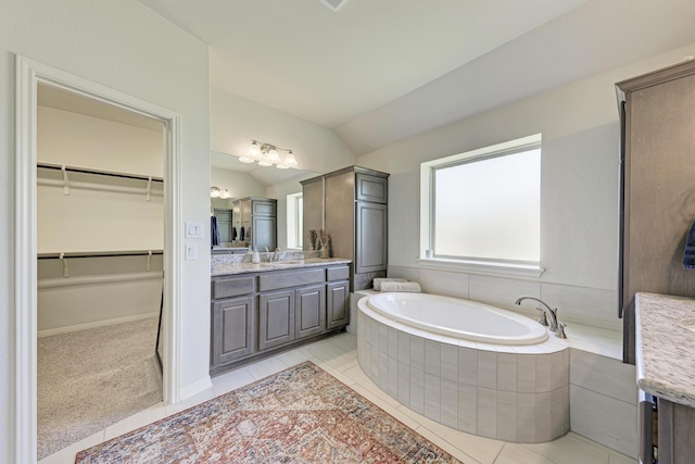 bathroom featuring vanity, lofted ceiling, a relaxing tiled tub, and tile patterned floors