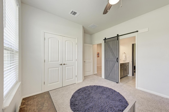 carpeted bedroom with a barn door, ensuite bath, ceiling fan, and a closet