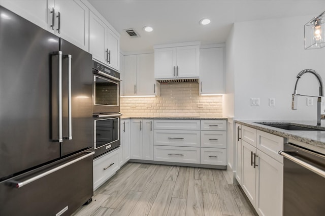 kitchen with stainless steel appliances, light stone countertops, sink, and white cabinets