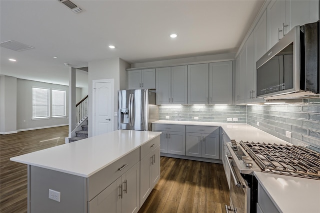 kitchen featuring stainless steel appliances, a kitchen island, dark hardwood / wood-style floors, and backsplash