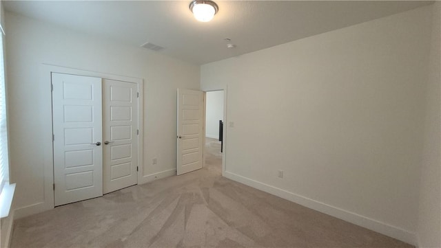 unfurnished bedroom with light colored carpet and a closet