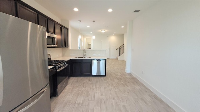 kitchen featuring appliances with stainless steel finishes, decorative light fixtures, tasteful backsplash, sink, and light hardwood / wood-style flooring