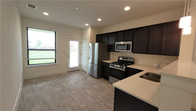 kitchen with appliances with stainless steel finishes, decorative light fixtures, light hardwood / wood-style floors, and sink