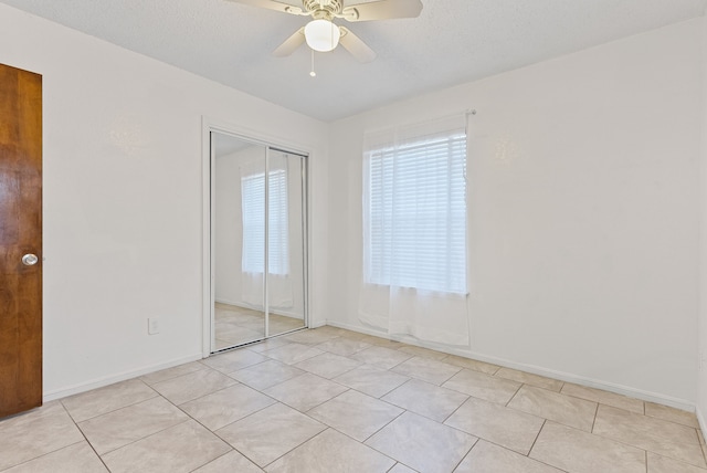 unfurnished bedroom featuring light tile patterned floors, a textured ceiling, a closet, and ceiling fan