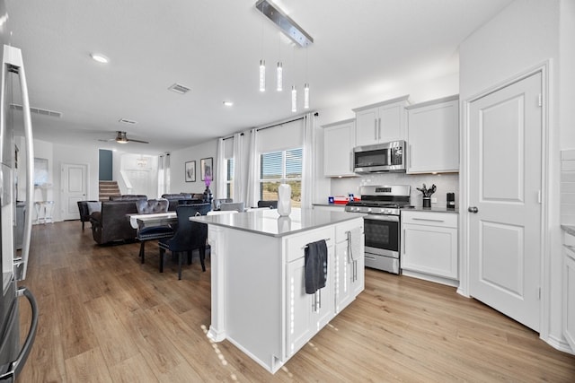 kitchen with pendant lighting, white cabinetry, a center island, stainless steel appliances, and light hardwood / wood-style flooring